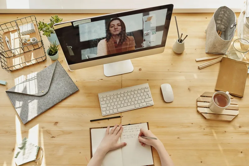 A desktop video call above an open notebook on a wooden desk.