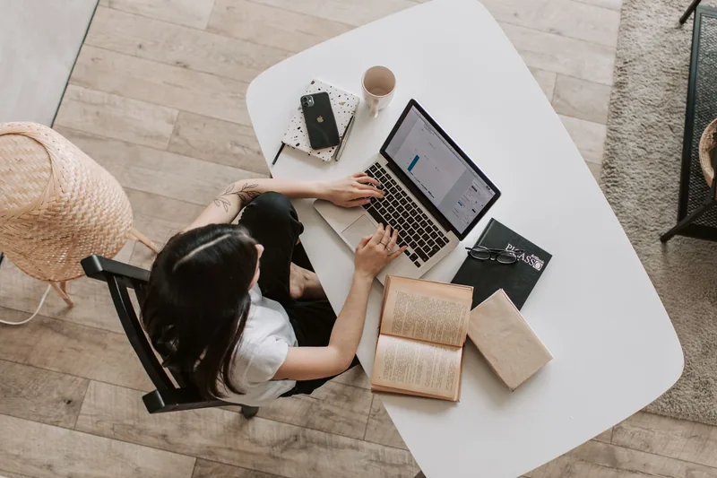 Overhead view of an adult using a laptop beside books at a round table.
