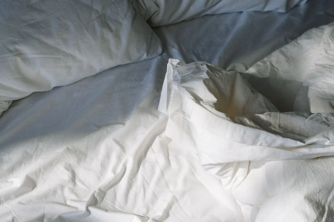 Soft white bed linen and pillows in gentle daylight.