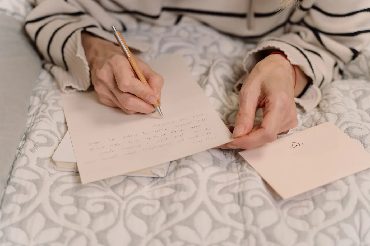 Hands writing a personal letter on paper beside an envelope.